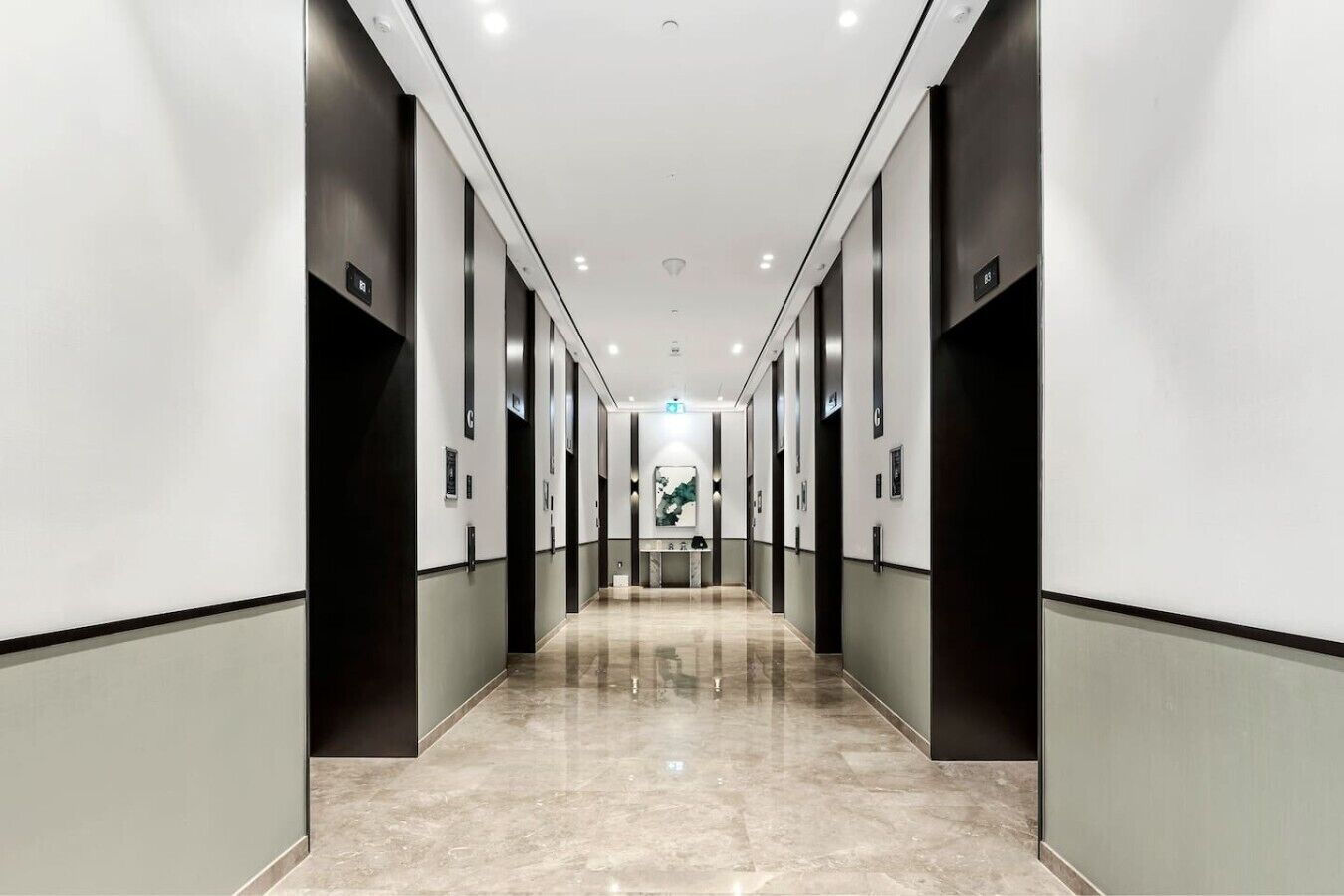 Ein moderner Hotelkorridor mit Marmorboden, schwarz-weißen Wänden und einem zentral platzierten Kunstwerk.