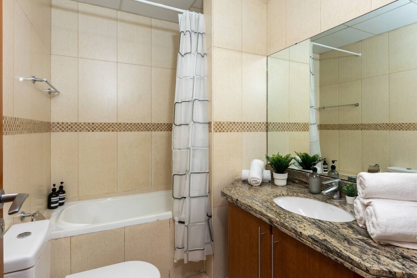 A bathroom with a bathtub, a shower curtain, a sink, a mirror, and toiletries.