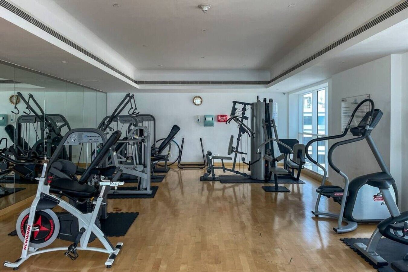 Ein Fitnessraum mit unterschiedlichen Trainingsgeräten, einem großen Spiegel und einem Holzboden.