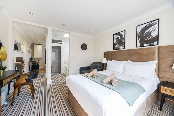 A hotel room with a large bed, a desk, a chair, a sofa, and artwork on the walls.