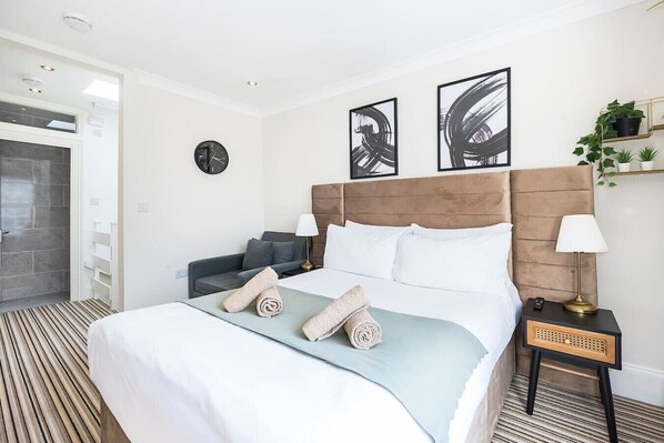 Une chambre d’hôtel avec un lit, un canapé, une horloge murale, des œuvres d’art abstraites et une petite plante.