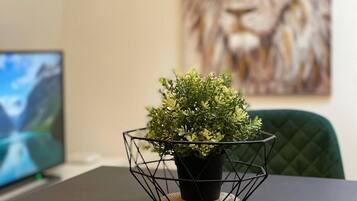 A potted plant in a wire basket on a table with a computer monitor and a painting in the background.