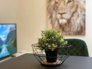 En potteplante i en wirekurv på et bord med en computerskærm og et billede i baggrunden.