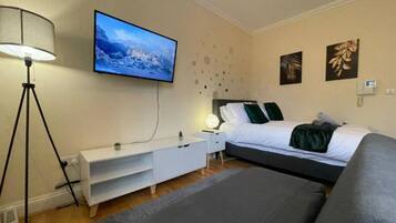 A bedroom with a bed, a TV mounted on the wall, a bedside table, a lamp, and a sofa.