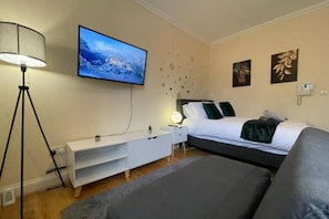 Et soveværelse med en seng, et tv på væggen, et natbord, en lampe og en sofa.