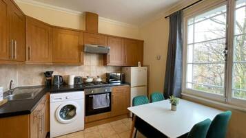 A compact kitchen with wooden cabinets, a washing machine, a stove, and a dining table with chairs.