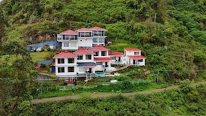 Un edificio residencial de varios pisos con techo rojo, rodeado de abundante vegetación y colinas.