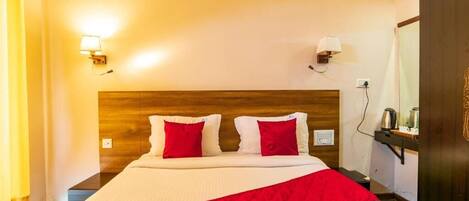 Une chambre d’hôtel avec une tête de lit en bois, un lit avec une literie blanche et des oreillers rouges, une couverture rouge, deux lampes fixées au mur et une armoire en bois foncé.