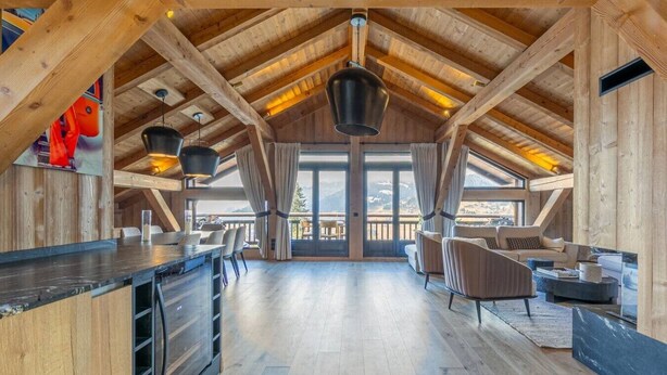 A spacious loft-style room with a high ceiling, wooden beams, a large window, and a dining area. - Stunning 5-bedroom chalet in Mont d'Arbois (Megève)