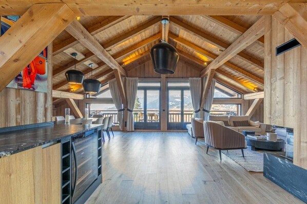 A spacious loft-style room with a high ceiling, wooden beams, a large window, and a dining area.