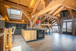A spacious interior with a wooden ceiling, a kitchen area, and a dining space with chairs.