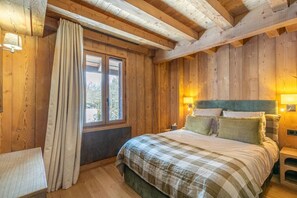 A wooden room with a bed, two bedside lamps, a window with curtains, and a small table.