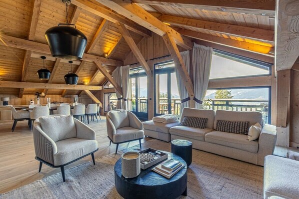 A spacious loft-style room with high ceilings, exposed wooden beams, and large windows offering mountain views.