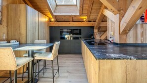 A modern kitchen with wooden beams, a skylight, and a dining area with a table and chairs. - Stunning 5-bedroom chalet in Mont d'Arbois (Megève)
