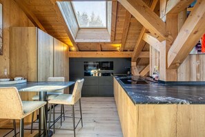 A modern kitchen with wooden beams, a skylight, and a dining area with a table and chairs. - Stunning 5-bedroom chalet in Mont d'Arbois (Megève)