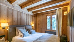 A wooden cabin bedroom with a bed, bedside lamps, and a window with curtains. - Stunning 5-bedroom chalet in Mont d'Arbois (Megève)