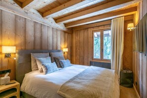 A wooden cabin bedroom with a bed, bedside lamps, and a window with curtains. - Stunning 5-bedroom chalet in Mont d'Arbois (Megève)