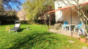 Un jardin avec une pelouse, un fauteuil de relaxation, une table et un espace abrité avec des chaises.