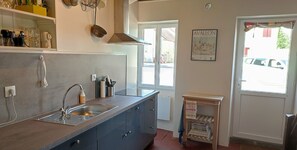 A kitchen with a sink, cabinets, a hanging pot rack, and a small wooden shelf with towels.