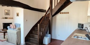 A staircase with wooden railings, a sofa with striped cushions, a fireplace, and a kitchen area with a sink and microwave.