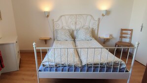 Un lit avec un cadre en métal, deux tables de chevet, une chaise et un luminaire fixé au mur.