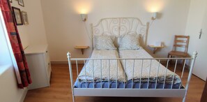 Un lit avec un cadre en métal, deux tables de chevet, une chaise et un luminaire fixé au mur.