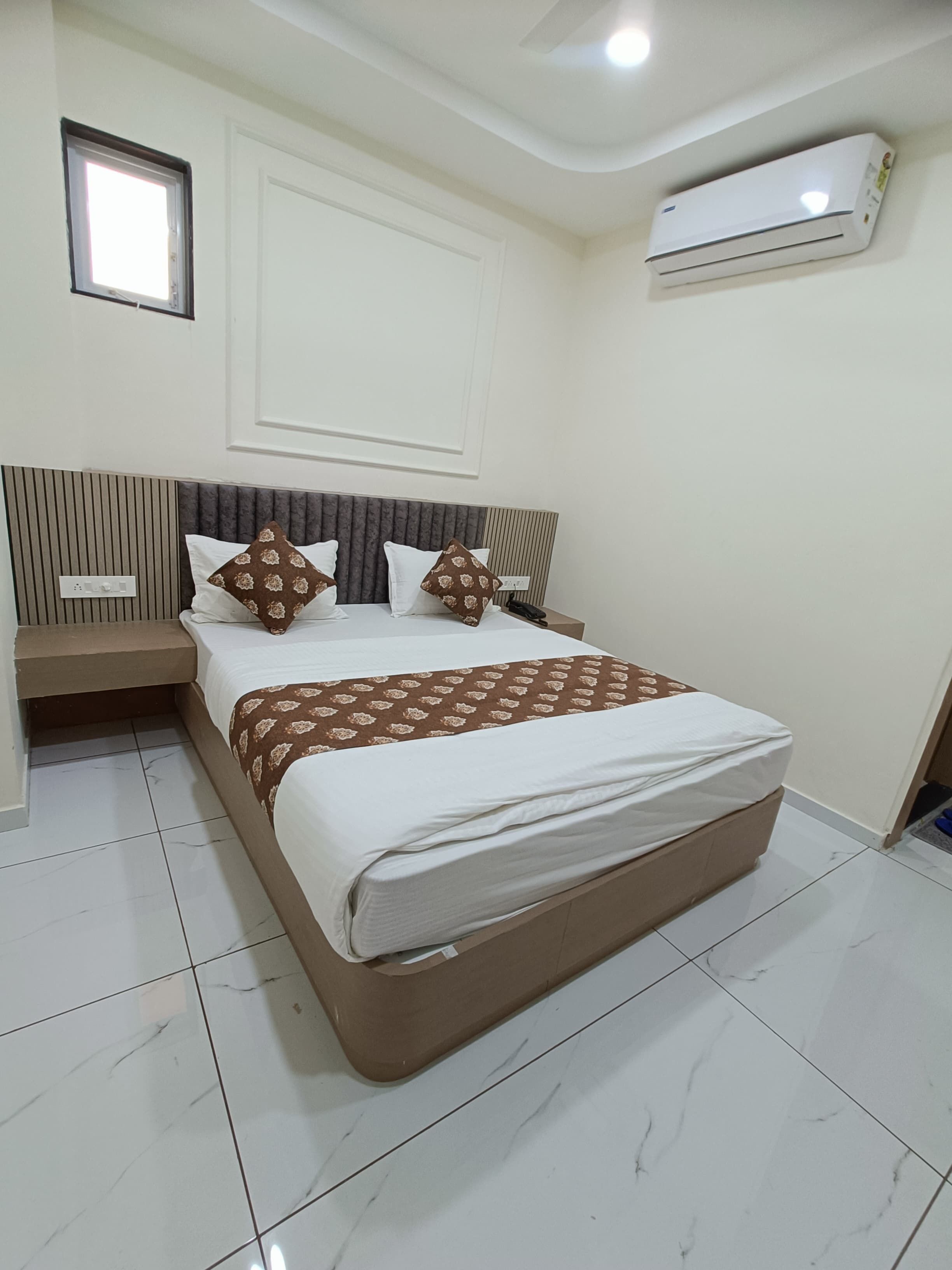 A neatly arranged bedroom with a bed, bedside tables, an air conditioning unit, and a window.