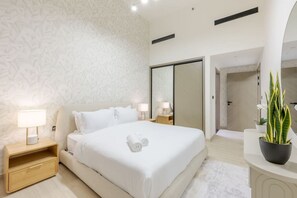 A modern hotel room with a large bed, bedside tables with lamps, a wardrobe, a mirror, and a potted plant. - FIRST CLASS | 1BR | Serenity Escape in JVC (JVC)