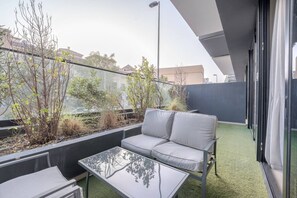 A balcony with a sofa, a glass table, and plants. - FIRST CLASS | 1BR | Serenity Escape in JVC (JVC)