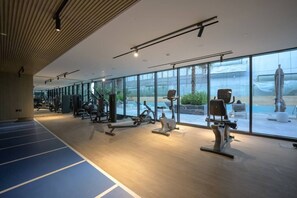 A modern gym with various exercise equipment, large windows, and a wooden ceiling. - FIRST CLASS | 1BR | Serenity Escape in JVC (JVC)
