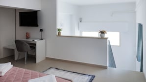 Une chambre à coucher avec un lit, un bureau, une chaise, une télévision, une fenêtre et une petite plante.