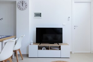 Una sala de estar moderna con un televisor de pantalla plana sobre un mueble de madera, sillas blancas, un reloj y una puerta.