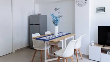A modern kitchen with a dining table, chairs, a refrigerator, a clock, and a television.