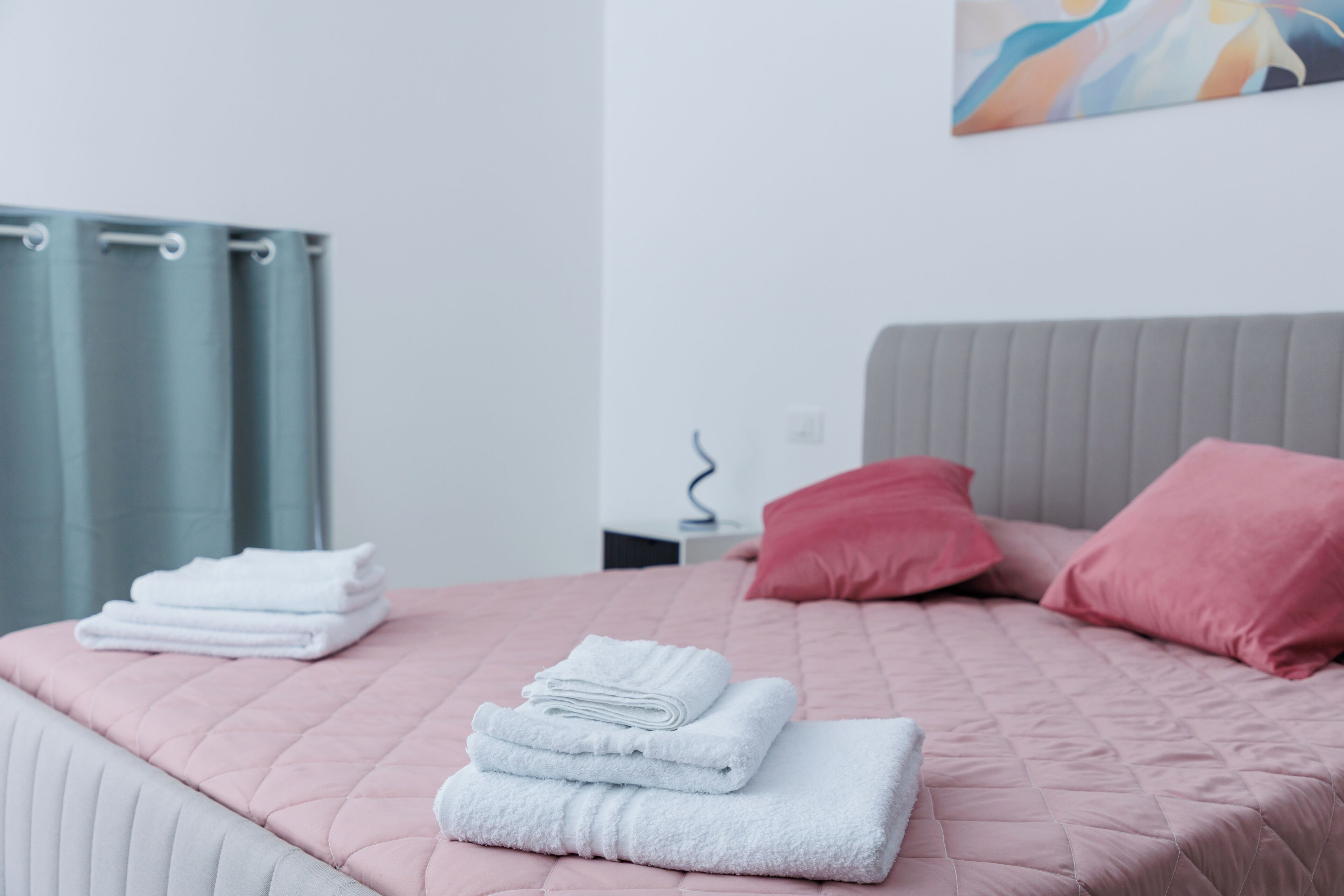 Ein ordentlich bezogenes Bett mit rosa Bettwäsche, ein Stapel weißer Handtücher und zwei rote Kissen.