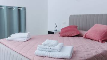 Ein ordentlich bezogenes Bett mit rosa Bettwäsche, ein Stapel weißer Handtücher und zwei rote Kissen.