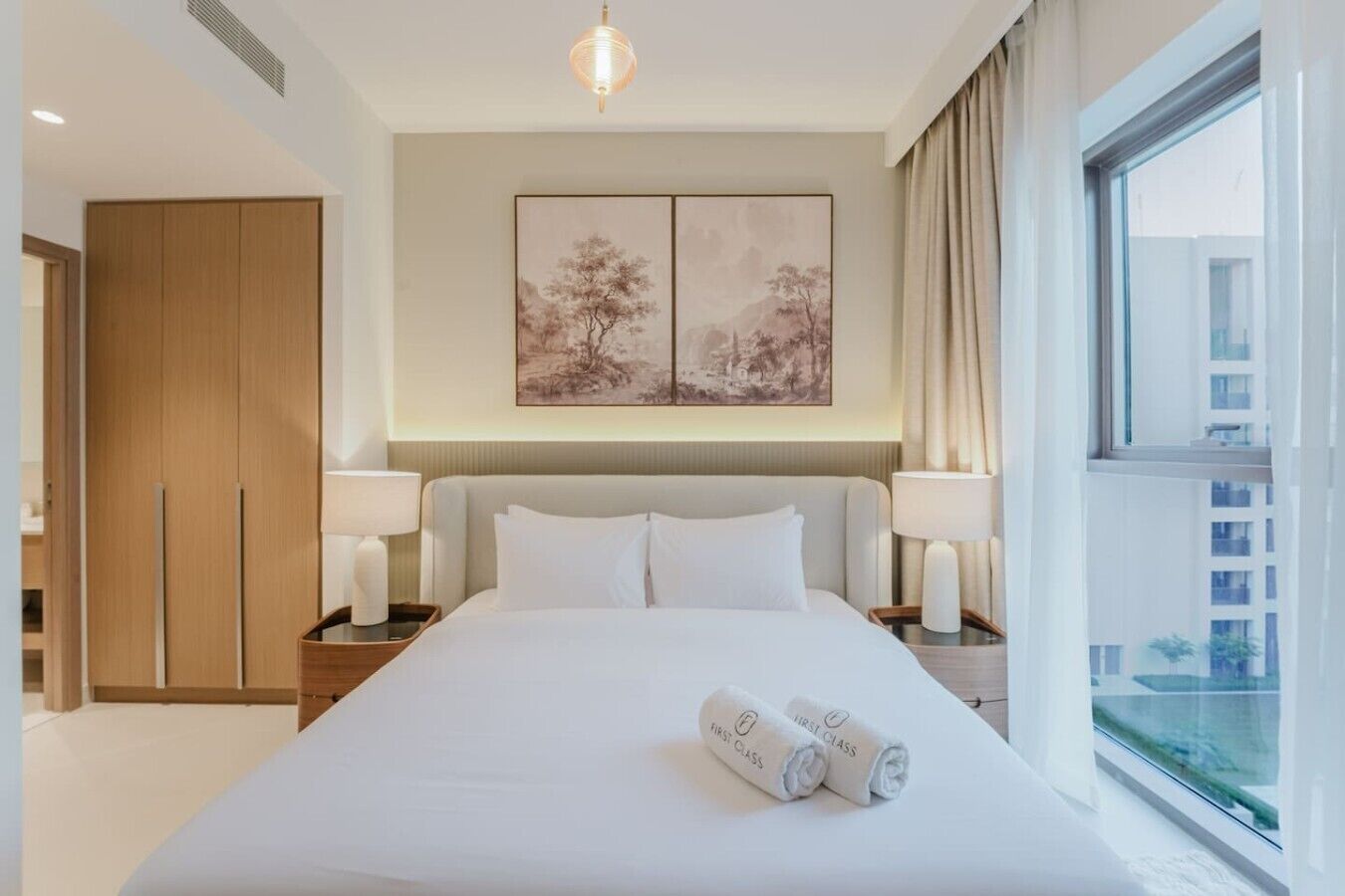 Ein Hotelzimmer mit einem großen Bett, zwei Nachttischlampen, Blick auf die Stadt und einem Bild an der Wand.