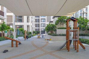 A children's play area with swings, a slide, and a climbing structure. - FIRST CLASS | 2BR | Relax & Unwind | Creek Beach (Dubai Creek Harbour)