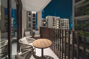 A balcony with wicker chairs, a round table, and a view of modern buildings at night. - FIRST CLASS | 2BR | Relax & Unwind | Creek Beach (Dubai Creek Harbour)