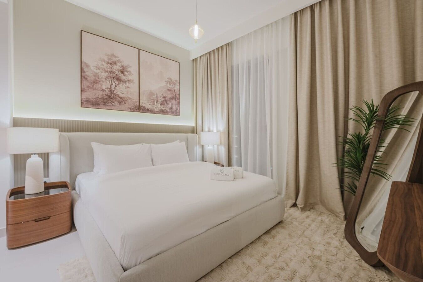 Une chambre d’hôtel bien rangée, avec un grand lit, des tables de chevet, un miroir et un tableau accroché au mur.