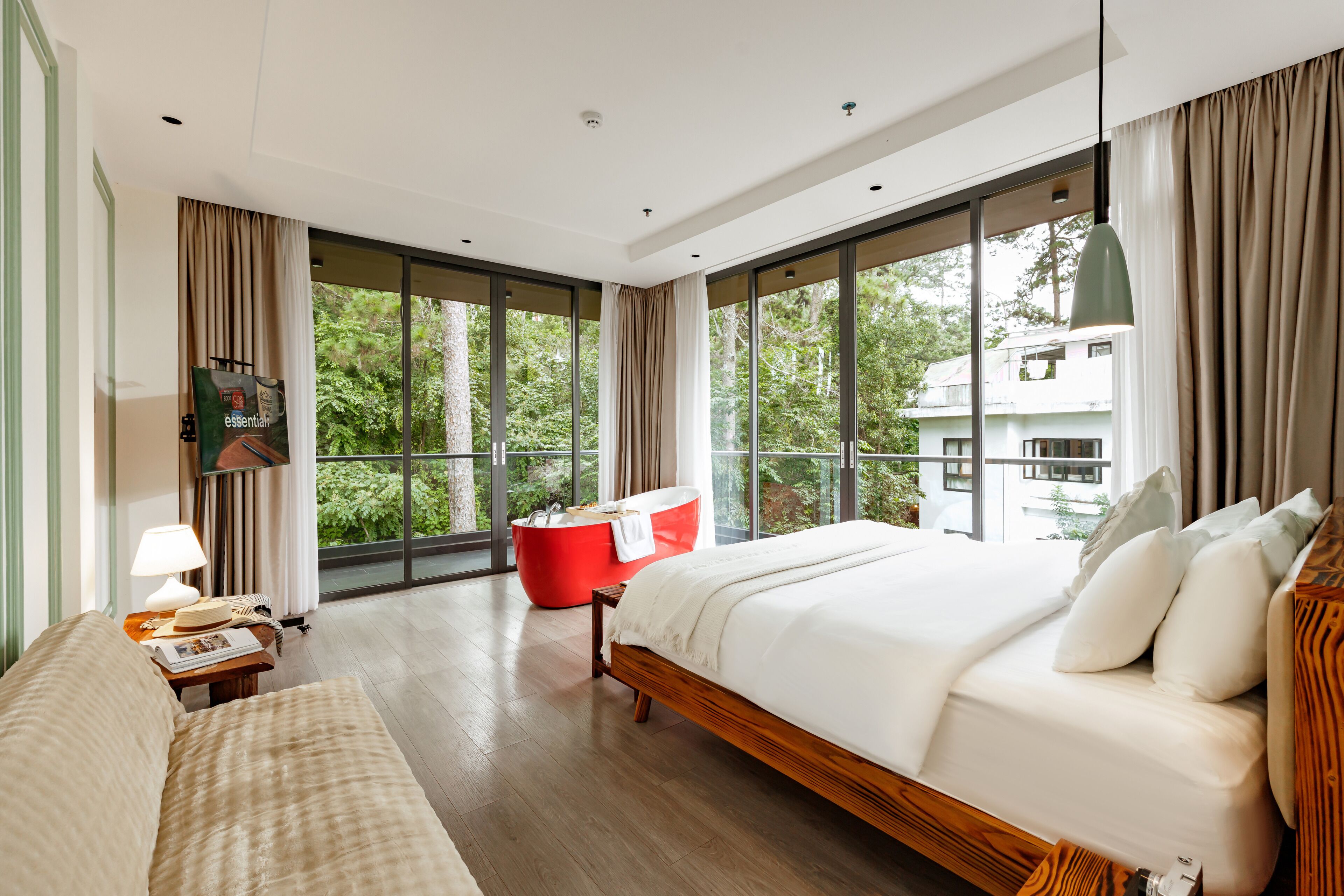 A modern hotel room with a large bed, a red bath tub, and a view of the outdoors.