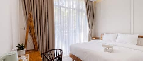 A hotel room with a bed, a wooden desk, a chair, a coffee maker, and a window with curtains.
