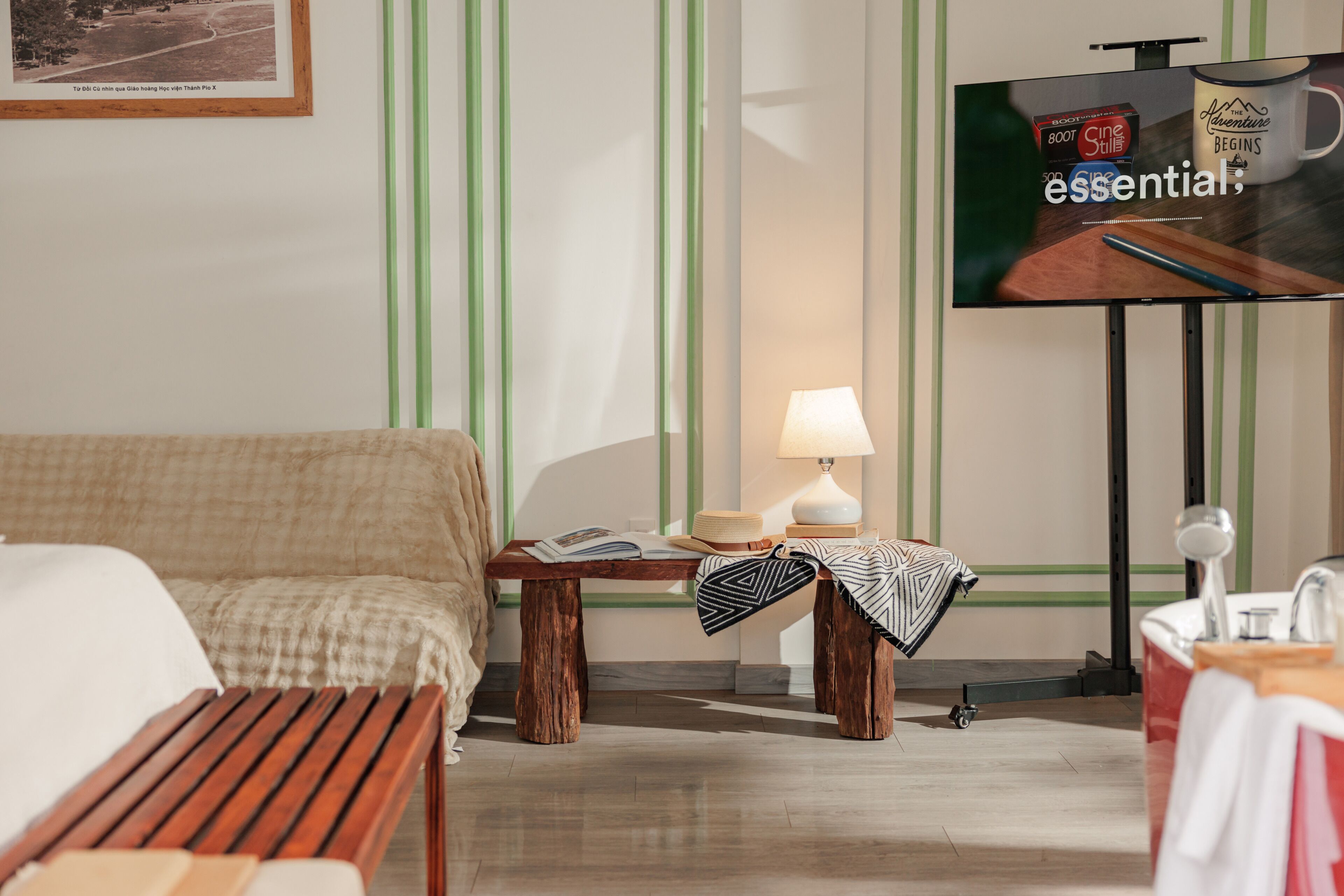 A hotel room with a bed, a small table with a lamp, a TV, and a wall-mounted shelf.