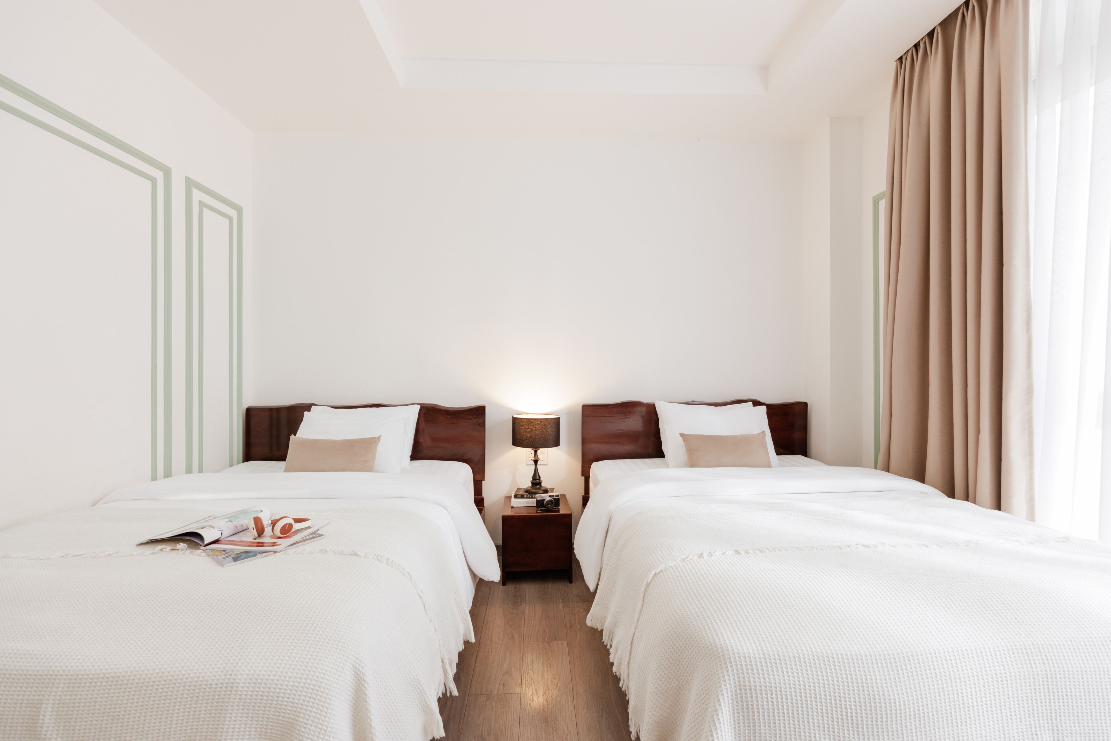 A hotel room with two beds, a nightstand with a lamp, and a window with curtains.