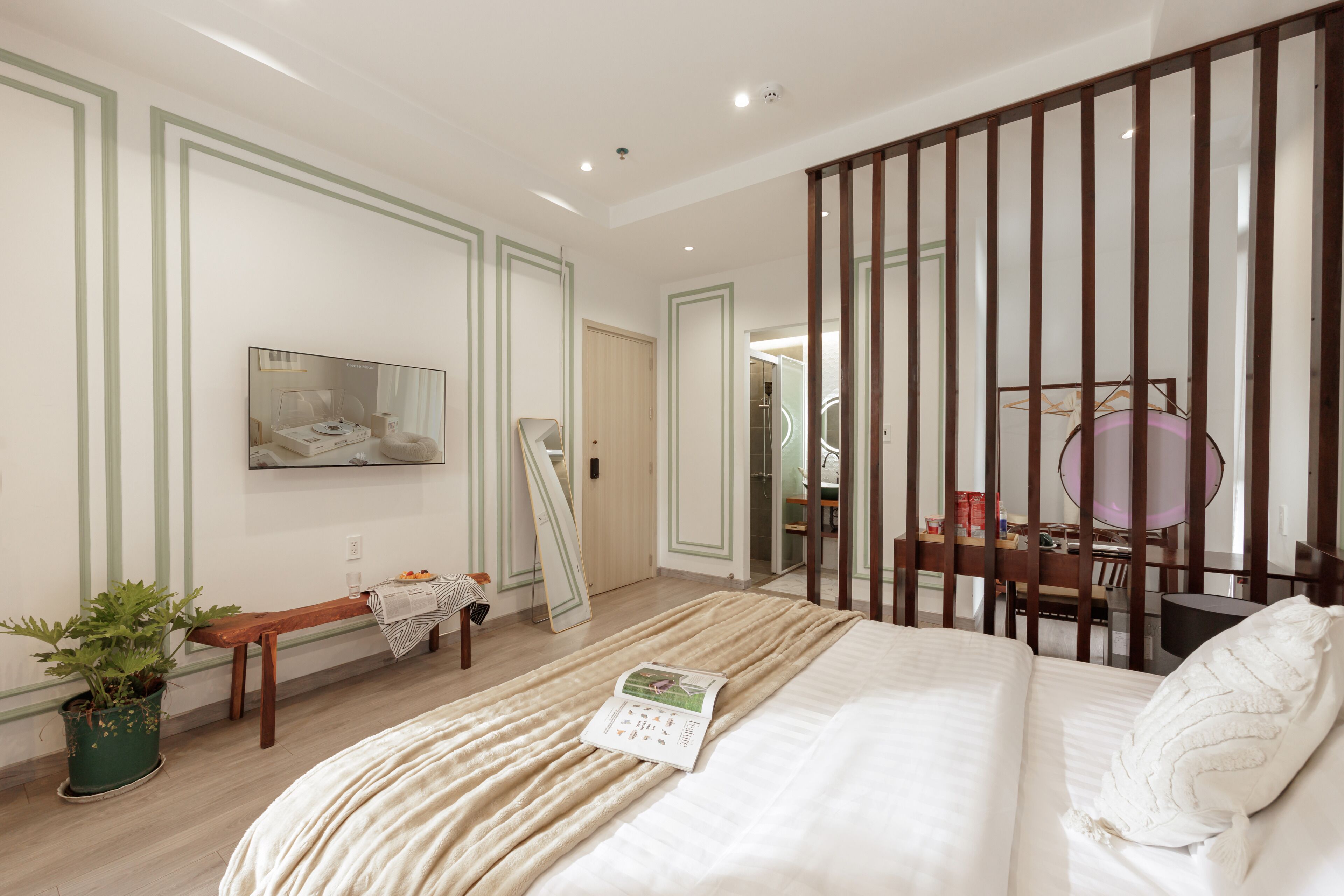 A modern bedroom with a large bed, a bedside table, a mirror, and a window with blinds.