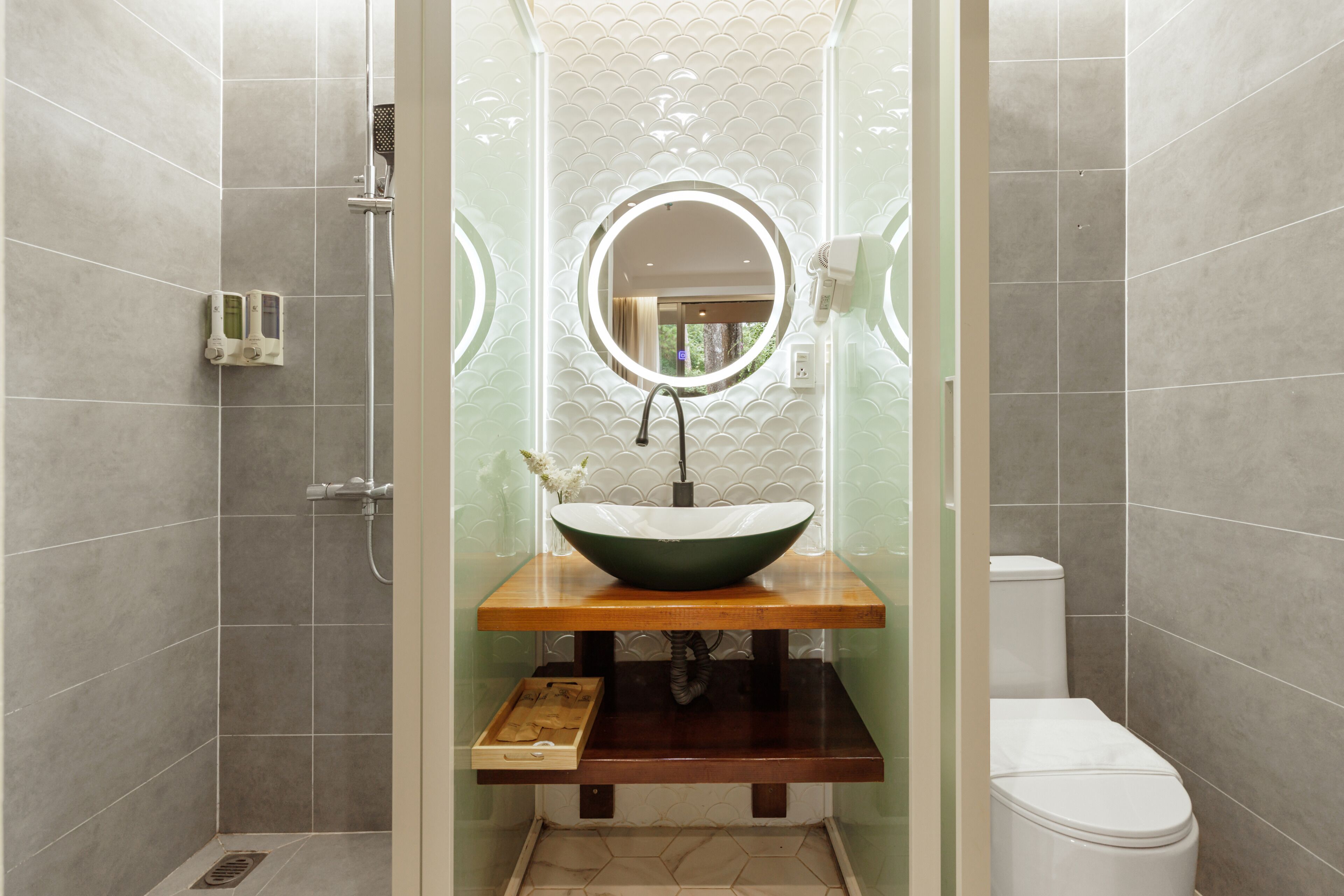 A modern bathroom with a glass-enclosed shower, a wooden vanity with a green sink, and a toilet.