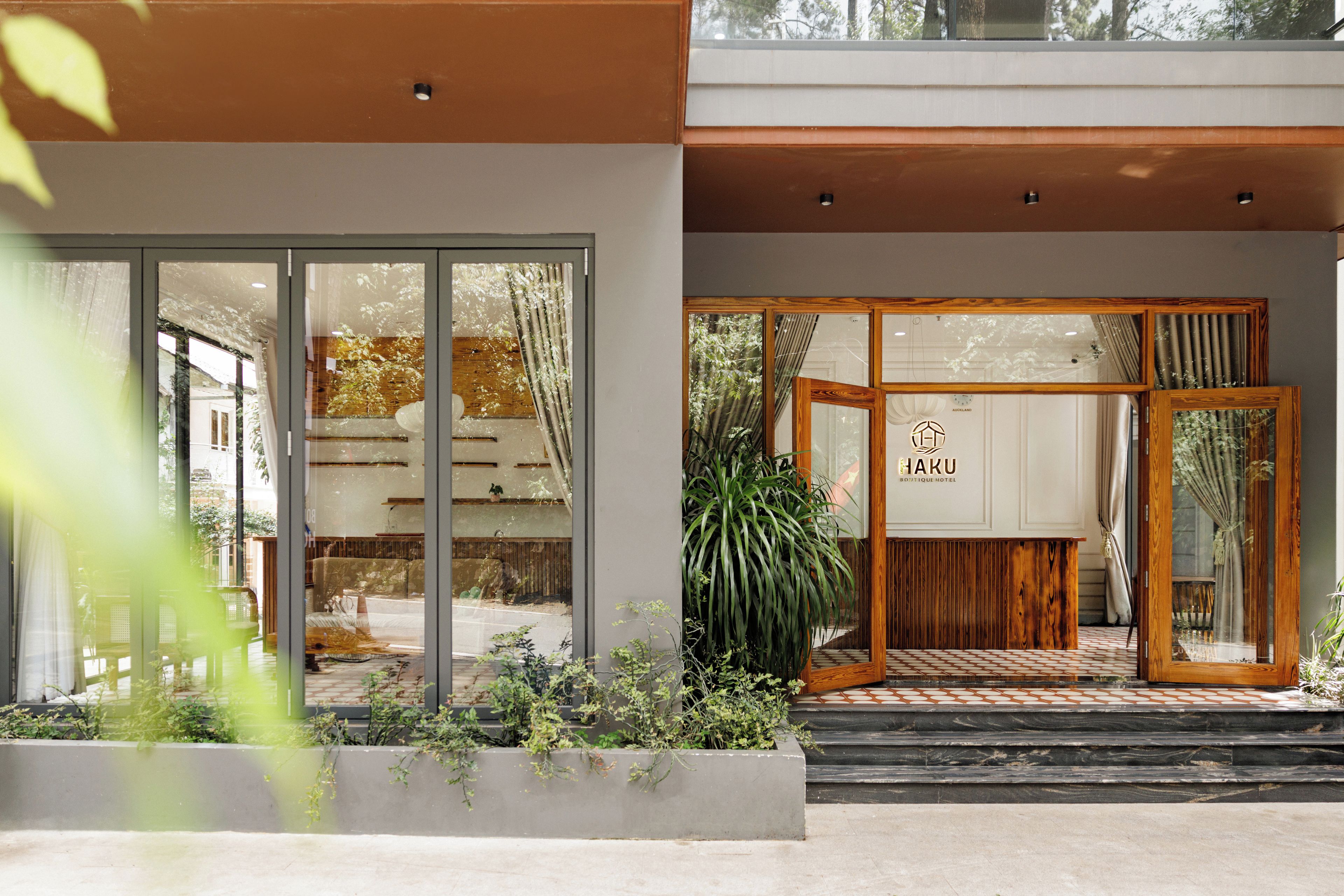 A hotel entrance with a wooden reception desk, a glass door, and a sign reading 'HAKU BOUTIQUE HOTEL'.