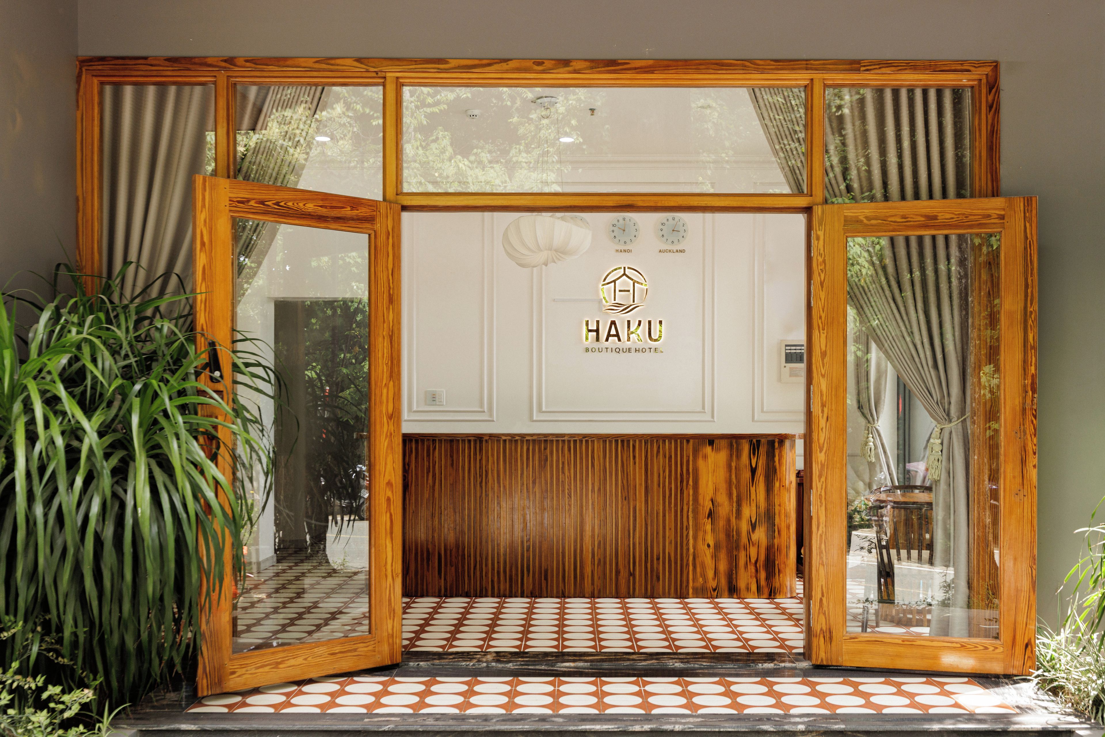 A hotel entrance with a wooden frame, a sign reading 'HAKU BOUTIQUE HOTEL,' and a tiled floor pattern.