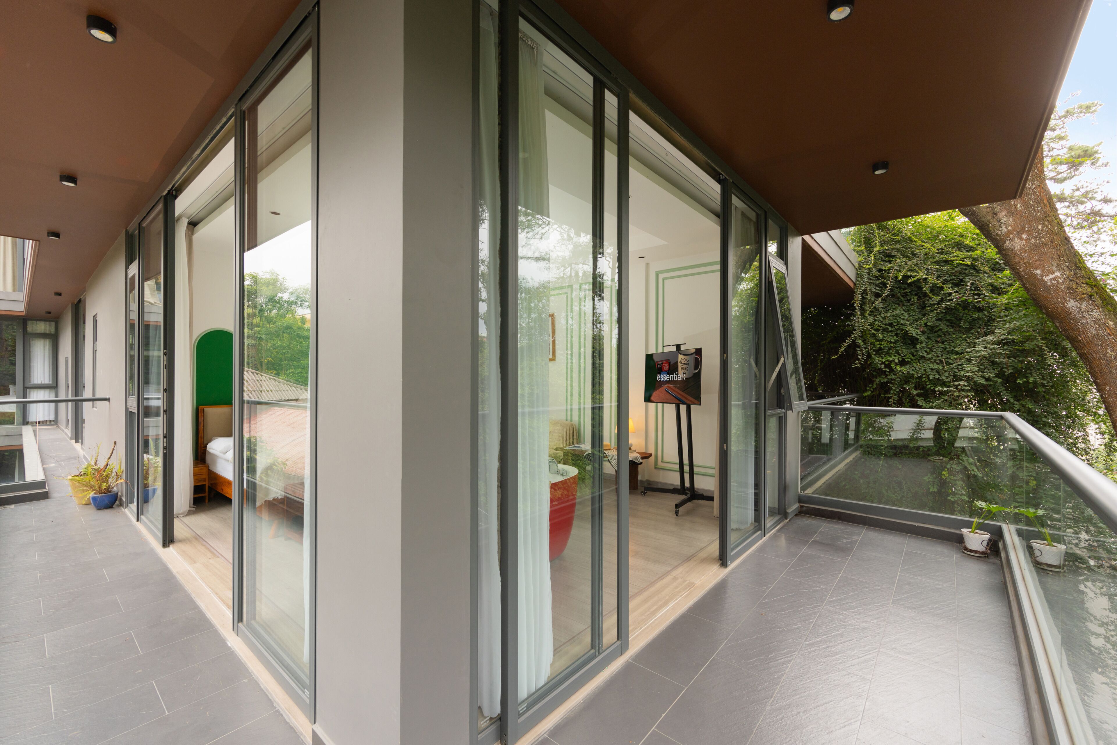 A modern hotel room with large glass doors, a balcony with a railing, and a view of the outdoors.