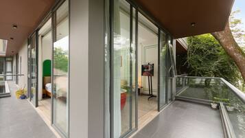 A modern hotel room with large glass doors, a balcony with a railing, and a view of the outdoors.