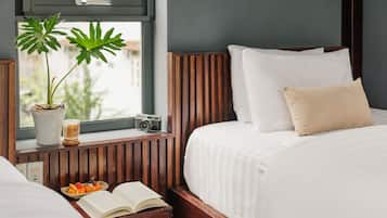 A hotel room with a bed, a bedside table with a book and decorative items, a potted plant, and a window with a view.